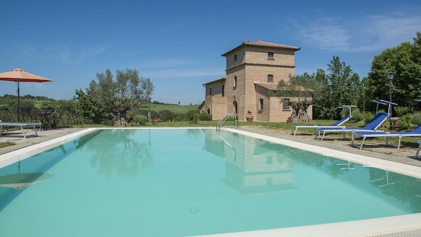 A swimming pool with lounge chairs and a stone building in the background. - Casale Cinque Valli 8 (Cortona)