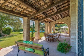 Un patio al aire libre con una pérgola de madera, columnas de ladrillo y una piscina al fondo.