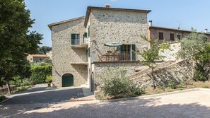 A two-story stone building with a balcony, a door, and a small garden area. - Casa Elia 4 2 in Palazzone (San Casciano dei Bagni)