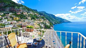 A balcony with a table set for dining, overlooking a coastal town with colorful buildings and a clear blue sea. - Casa Leonilde 4 in Positano (Positano)