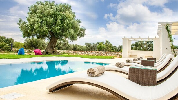 A poolside area with lounge chairs, a pergola, and a large tree. - White Stone House 6 1 (Ostuni)