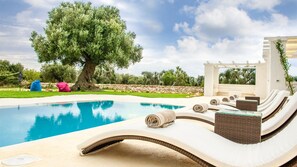 A poolside area with lounge chairs, a pergola, and a large tree. - White Stone House 6 1 (Ostuni)