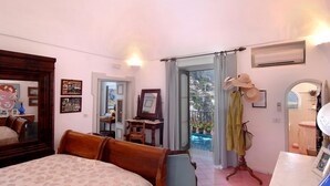Ein Schlafzimmer mit Bett, Schreibtisch, Stuhl, Kleiderschrank und einem Balkon mit Blick auf eine Stadt.