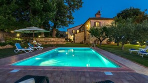 A rectangular swimming pool with a paved deck, surrounded by lounge chairs and a pergola.