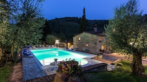 Un bâtiment en pierre doté d’une piscine, entouré d’arbres et situé au pied d’une colline.