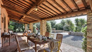 An outdoor patio with stone pillars, wooden furniture, and a view of the surrounding garden. - Virginia 8 in Gavorrano (Scarlino)