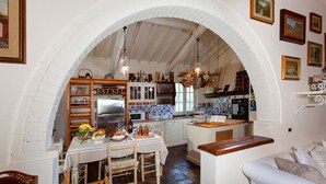 A cozy kitchen with an arched doorway, wooden cabinets, a refrigerator, and a dining table set with fruits and a book. - Virginia 8 in Gavorrano (Scarlino)