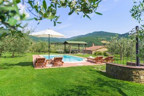 Uma área de piscina com espreguiçadeiras, um pérgola e um muro de pedra.