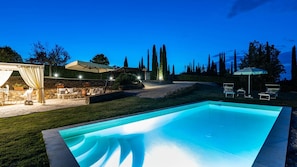 Ein Pool mit einer Steinterrasse, eine überdachte Terrasse mit Gartenmöbeln und ein gepflegter Rasen.
