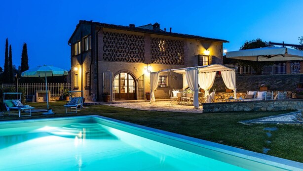 Une grande maison à deux étages, dotée d’une piscine, d’un espace extérieur aménagé pour se détendre et d’une terrasse bien éclairée.