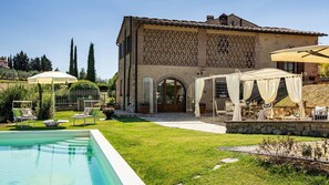 Eine Villa mit Swimmingpool, Sitzgelegenheiten im Freien und einem großen Bogenportal.