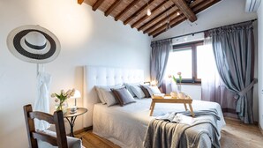Une chambre à coucher avec un grand lit, une chaise en bois, une petite table avec une lampe et une fenêtre avec des rideaux.