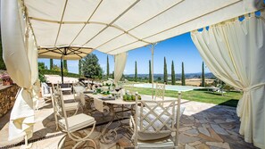 An outdoor dining area with a table set for four, surrounded by white chairs, under a large canopy. - Ricciolo 4 in San Gimignano (San Gimignano)