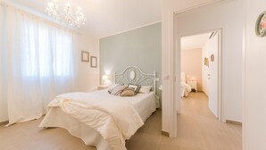 A bedroom with a bed, a chandelier, and a view into another room.