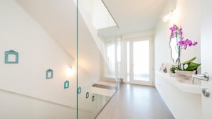 A modern interior with a glass staircase, white walls, and a door leading to another room.