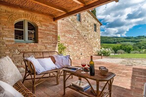 A rustic stone building with a brick patio, wicker furniture, and a bottle of wine.