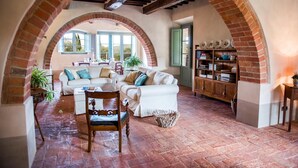 A spacious living area with a white sofa, a wooden chair, and a bookshelf. - Podere Pisinano 8 2 (Montepulciano)