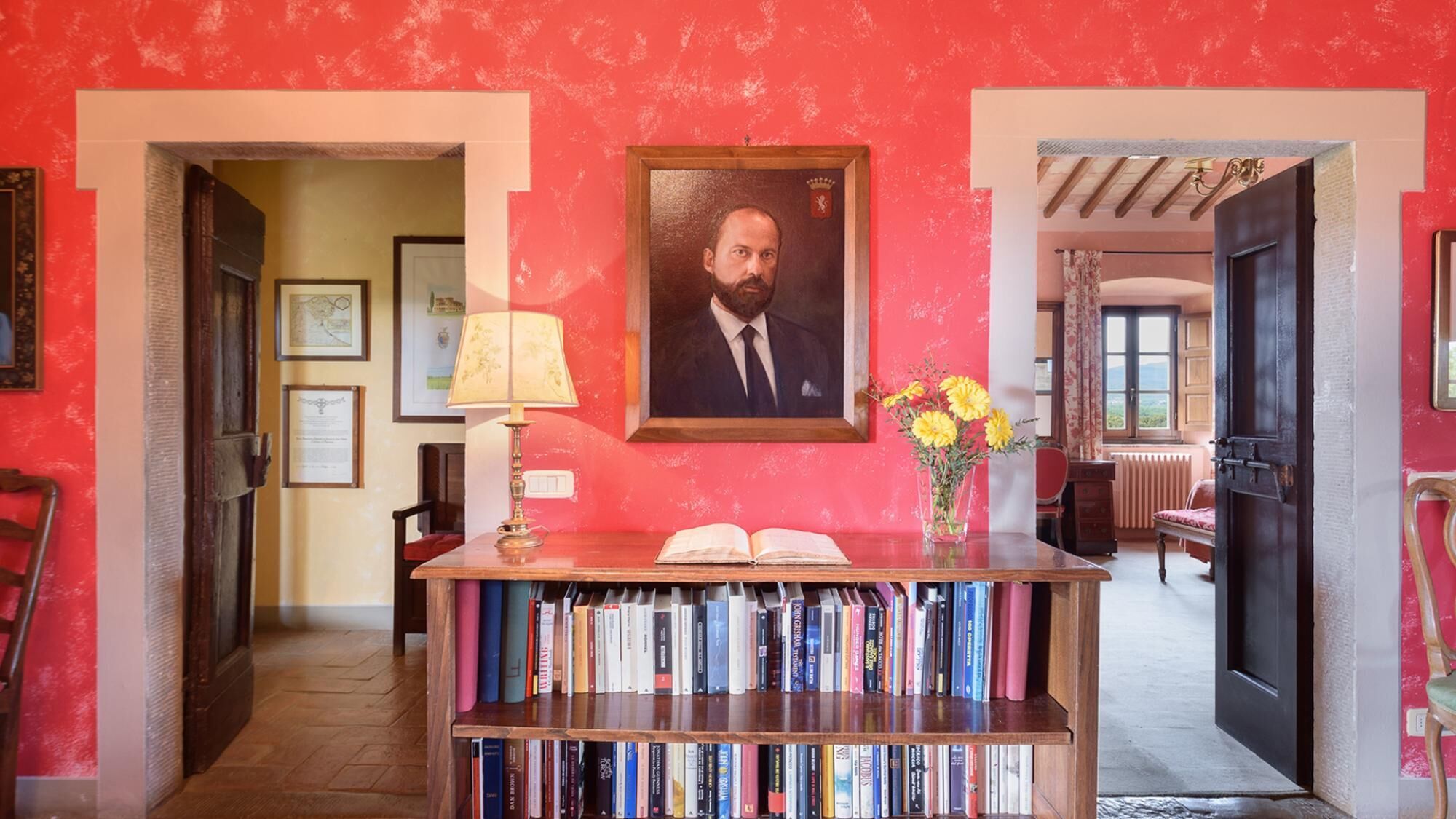 A hallway with a bookshelf, a framed portrait, and a vase with flowers.