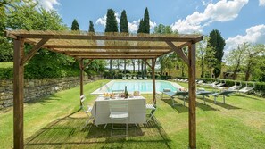 A poolside area with a pergola, lounge chairs, and a table set for a meal.