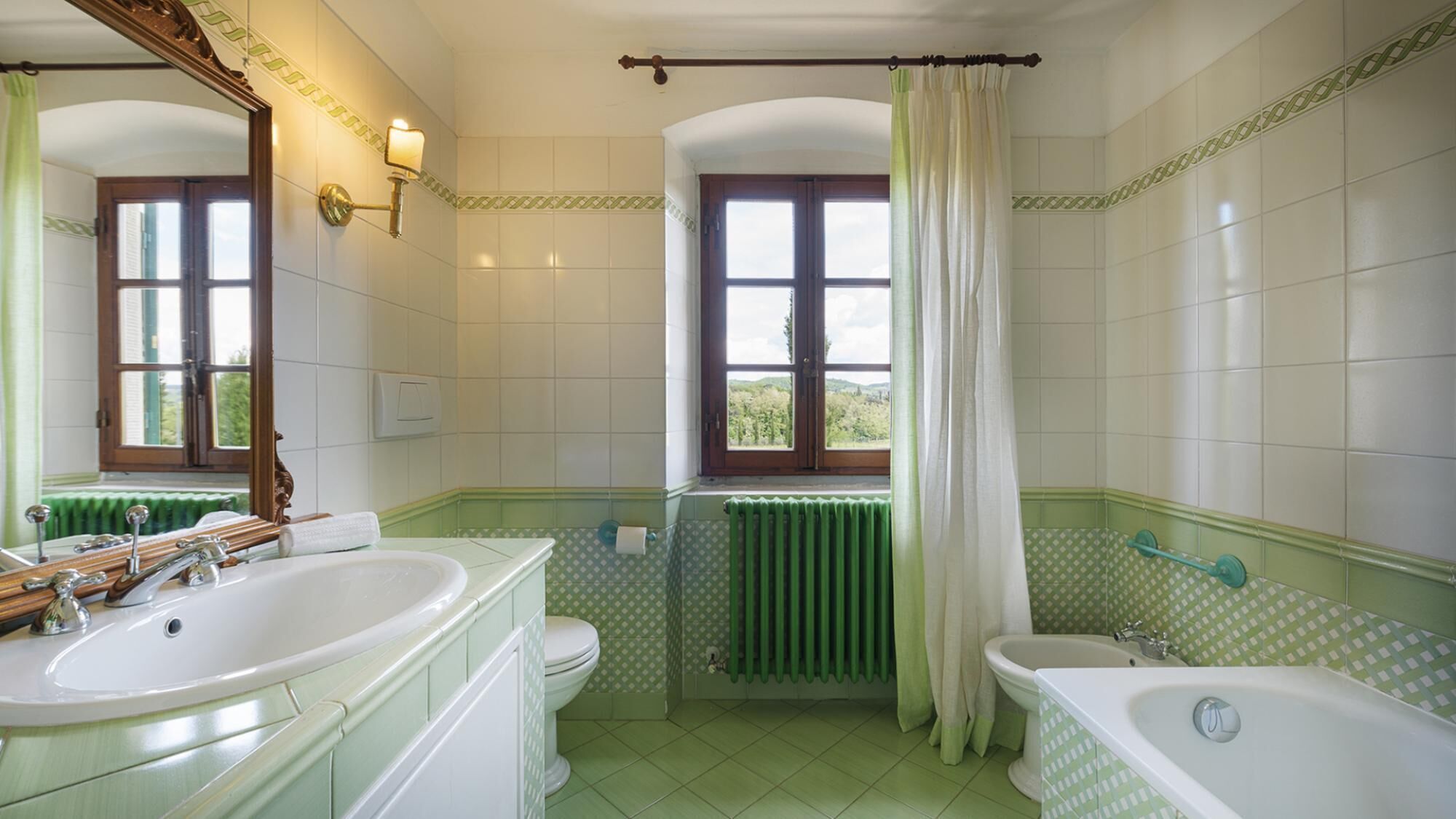 Un baño con dos lavamanos, una bañera y una ventana con vistas al verdor.