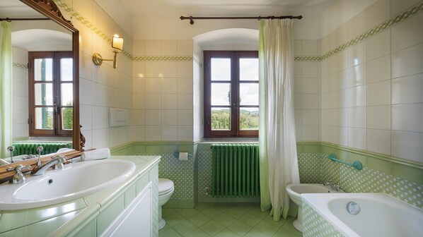 A bathroom with two sinks, a bathtub, and a window with a view of greenery.