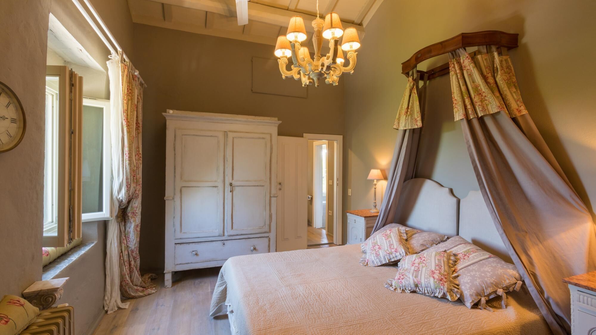 A bedroom with a large bed, a wardrobe, a chandelier, and a window with curtains.