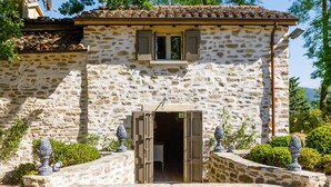 A stone building with a tiled roof, a central entrance with open shutters, and decorative urns on the steps. - Il Castellaccio 8 in Brisighella (Brisighella)