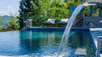 Una piscina con caída de agua, rodeada de muros de piedra y plantas en macetas.