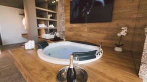 A spa room with a hot tub, wooden flooring, a TV mounted on the wall, and a bottle of champagne on the counter. - Villa Triscele 10 in Giardini Naxos (Giardini Naxos)