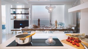A modern kitchen with a central island, a dining area with a chandelier, and a TV in the background. - Villa Triscele 10 in Giardini Naxos (Giardini Naxos)