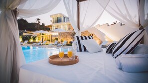 Cama con una bandeja de jugo de naranja y una botella, ropa de cama blanca y almohadas a rayas.