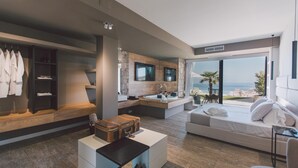 A modern bedroom with a large bed, a sitting area, a vanity with a bathtub, and a view of the ocean. - Villa Triscele 10 in Giardini Naxos (Giardini Naxos)