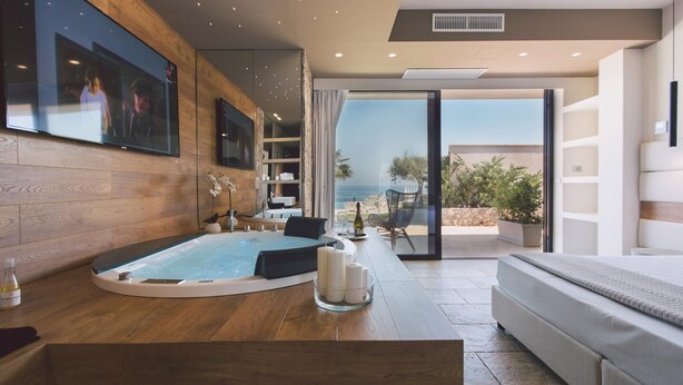 A modern room with a wooden floor, a large bathtub, a sofa, and a glass door leading to an outdoor area with a view of the sea. - Villa Triscele 10 in Giardini Naxos (Giardini Naxos)