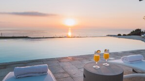 A sunset view over a pool with two glasses of orange juice on a table. - Villa Triscele 10 in Giardini Naxos (Giardini Naxos)