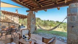 An outdoor patio with stone walls, wicker furniture, a hammock, and a table set with a bottle and fruit. - Montebendico 4 in Castel del Piano (Castel del Piano)