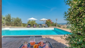 En swimmingpool med solstolar och parasoller, omgiven av grönska och en vacker utsikt.