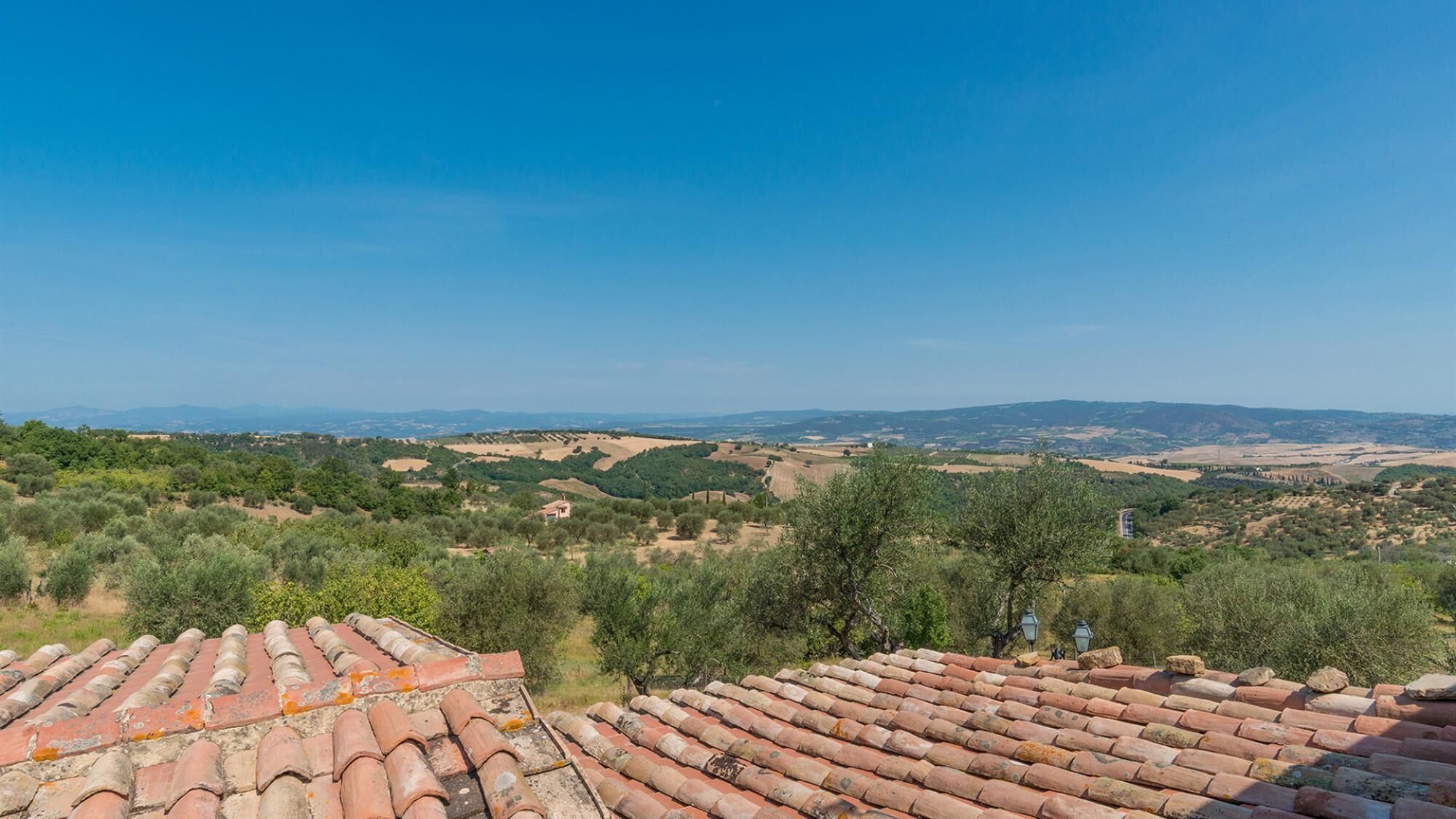 Un toit recouvert de tuiles en terre cuite, offrant une vue sur des collines ondoyantes et des montagnes lointaines.