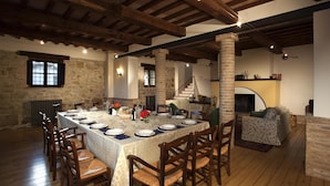 A dining area with a long table set for a meal, wooden chairs, stone walls, and a fireplace. - Il Borgo 16 in Assisi (Assisi)