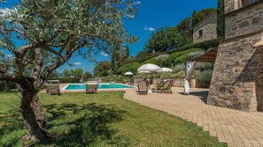Un área de piscina con sillones de descanso, una pérgola con sombrillas y muros de piedra.