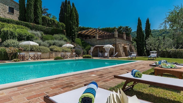 A pool area with lounge chairs and umbrellas, surrounded by greenery and stone buildings. - Il Borgo 16 in Assisi (Assisi)