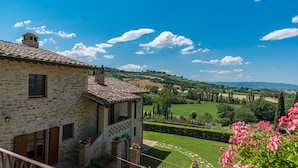 A stone building with a tiled roof, a small balcony, and a well-maintained garden with hedges and flowering plants. - Il Borgo 16 in Assisi (Assisi)