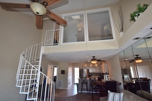 A spacious living area with a high ceiling, a central island, and a staircase leading to an upper level. - OVERSIZED Master Suite/Lakefront/Jetted tub/Main channel view- Cozy Fireplace! (Osage Beach)