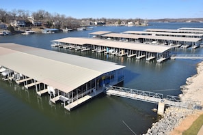 A marina with multiple docked boats, a covered pedestrian bridge, and a row of houses in the background. - OVERSIZED Master Suite/Lakefront/Jetted tub/Main channel view- Cozy Fireplace! (Osage Beach)