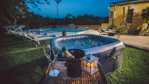 Un jacuzzi con una botella de champán y copas sobre una mesa, rodeado de sillones de descanso y una piscina al fondo.