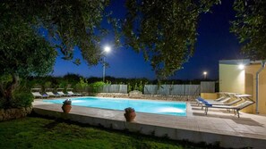 Una piscina con sillas de descanso y plantas en macetas, rodeada por un muro de piedra y árboles.
