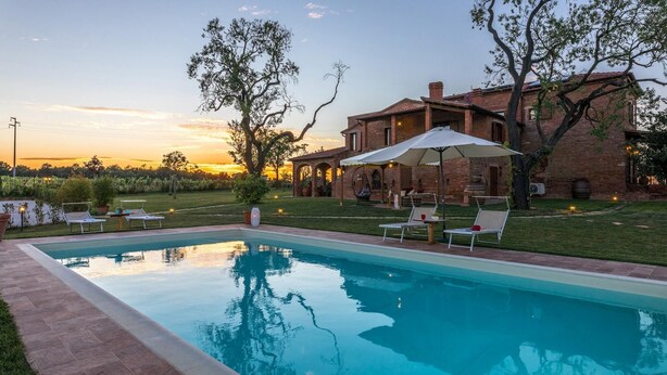 A swimming pool with lounge chairs and umbrellas, surrounded by a brick house with a patio.