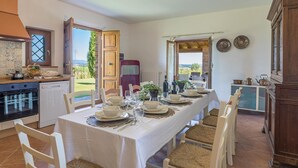 A dining area with a table set for six, kitchen appliances, and a view of the outdoors.