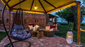 A cozy outdoor seating area with a hanging chair, a wooden table with cushions, and a lantern.