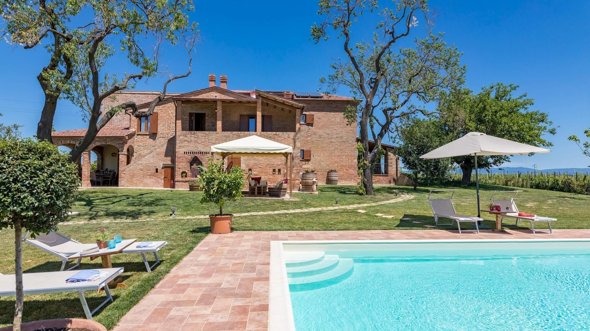 Una amplia casa de ladrillo con piscina, mobiliario exterior y vistas al paisaje.