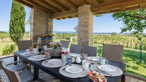 An outdoor dining area with a table set for four, surrounded by wicker chairs, under a wooden pergola.